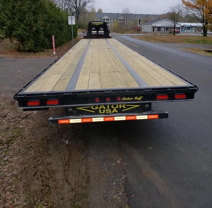 Une remorque à plateau est stationnée sur le bas-côté d'une route. Elle est recouverte de planches de bois et porte le logo de Gator USA.