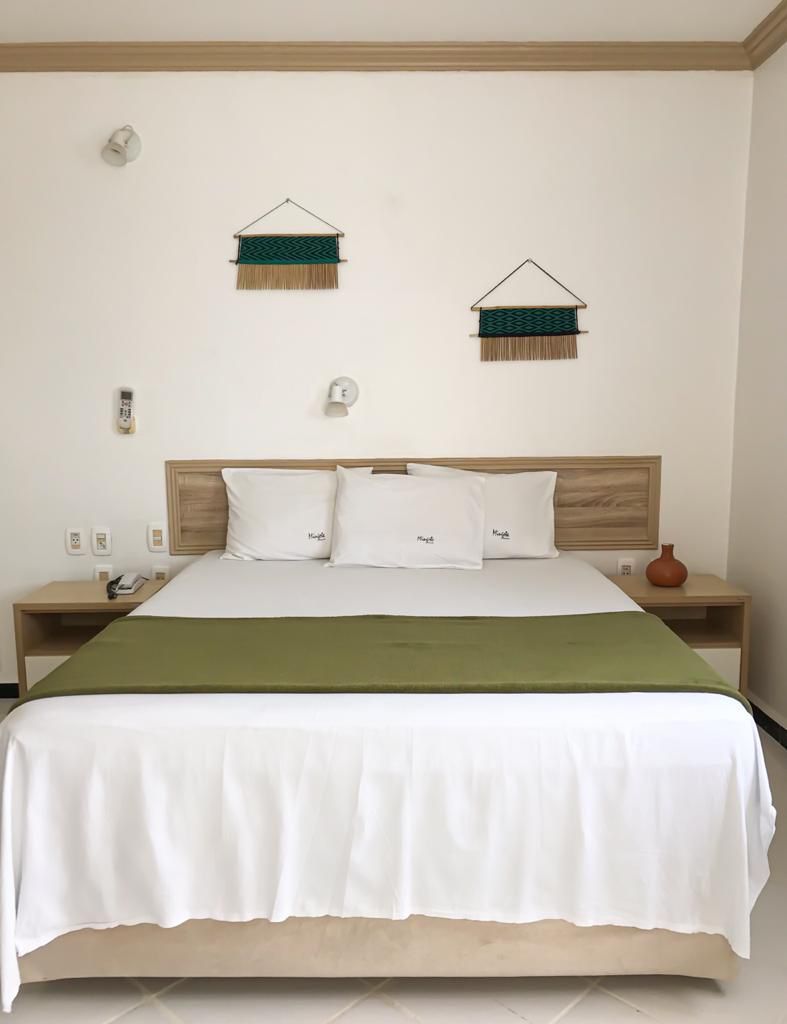 Uma cama com lençóis brancos e cobertores verdes em um quarto de hotel.