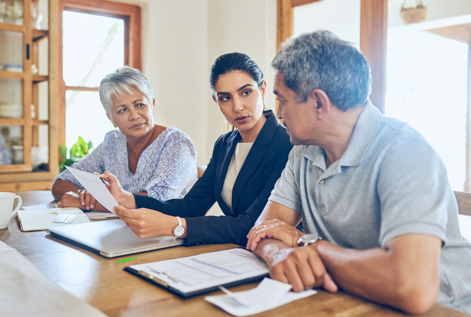 Three coworkers in a meeting at a wooden table, reviewing documents and discussing something intently.