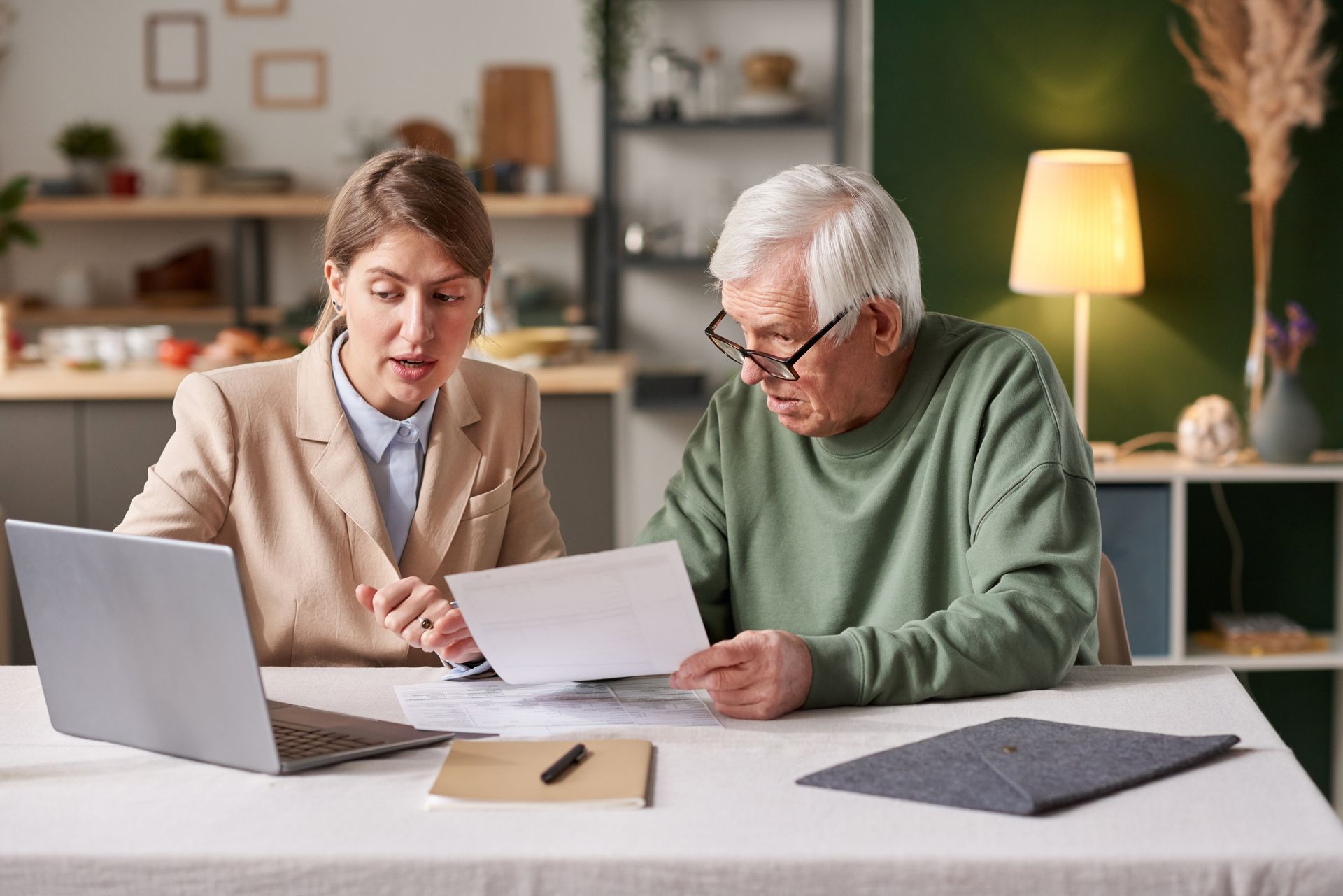 Two people reviewing documents at a table with a laptop in a cozy office space
