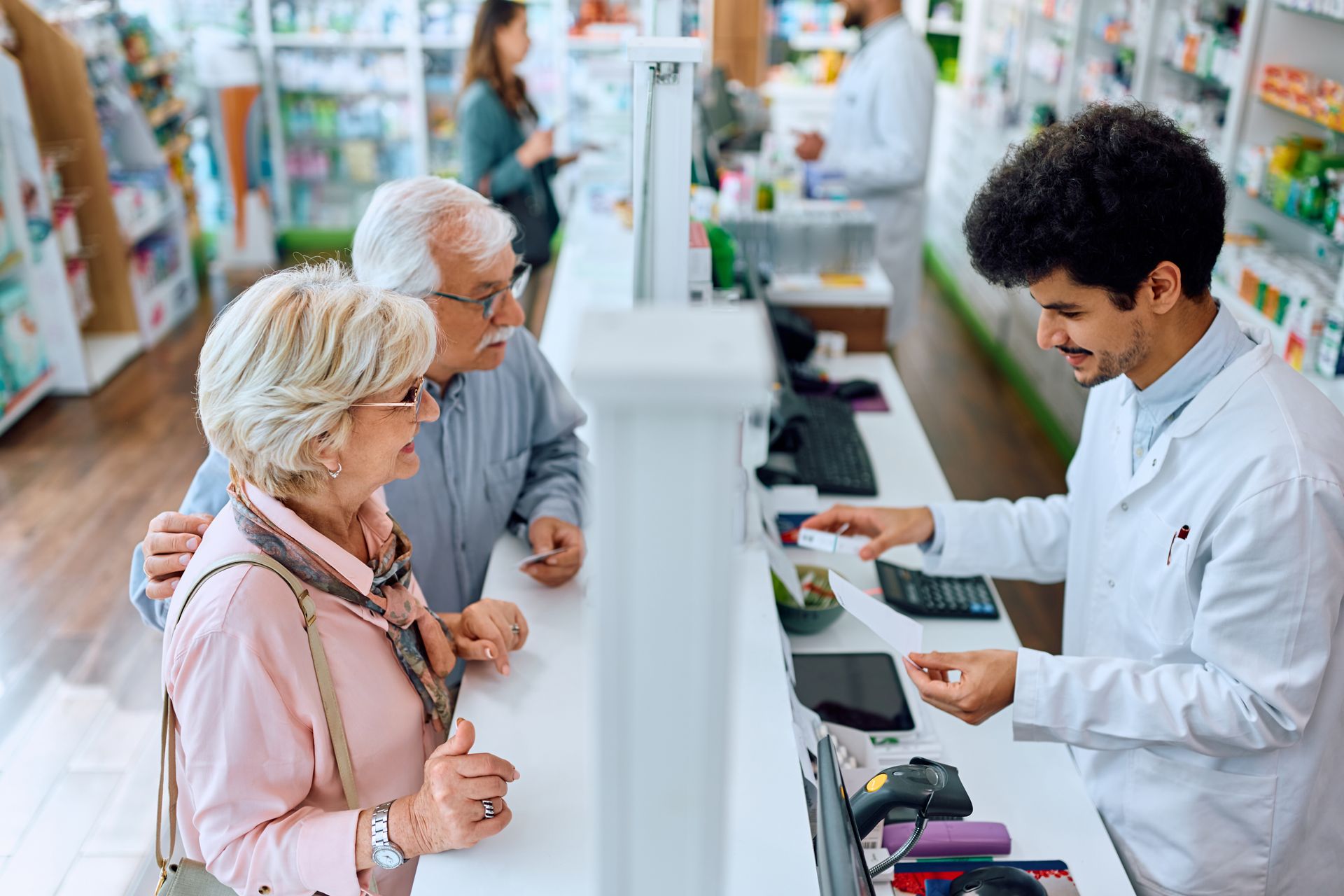 Pharmacist assisting customers at a pharmacy counter with a tablet and card terminal