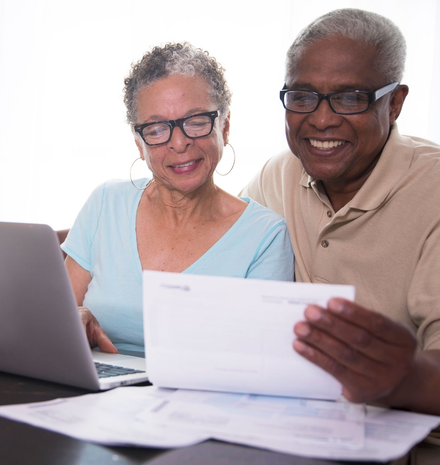 Two smiling seniors reviewing documents at a table with a laptop