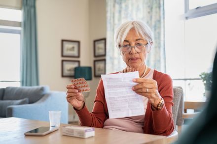 Woman at a table reading a bill while holding a credit card in a bright living room