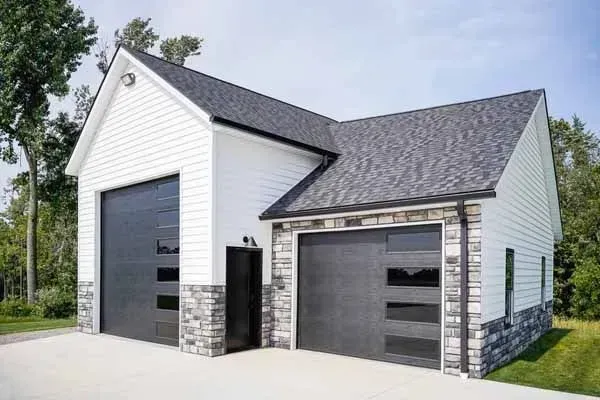 Two-car white garage with black doors and stone accents under a blue sky.