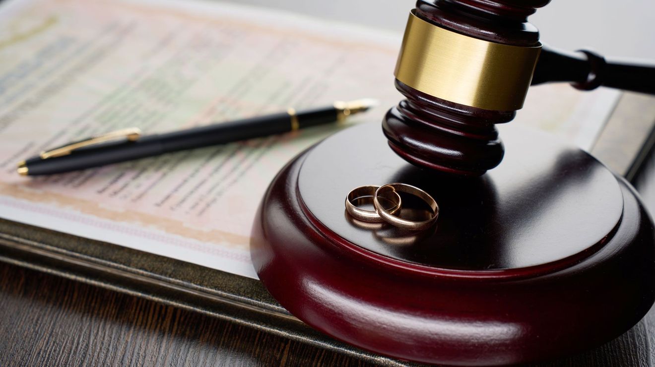 Gavel, wedding rings, and pen on a document, suggesting a marriage or divorce legal matter