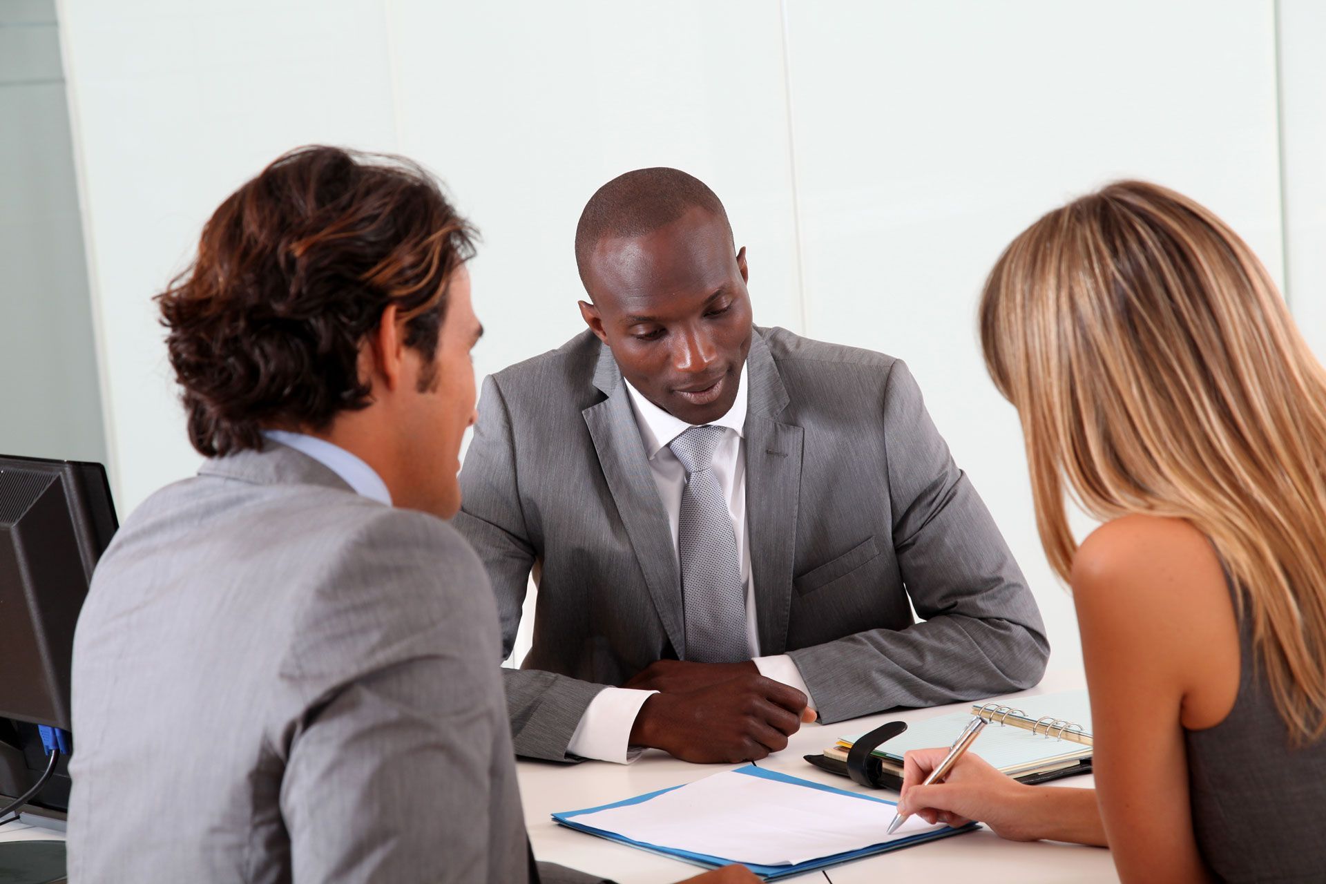 Three colleagues discuss documents at a meeting table in an office