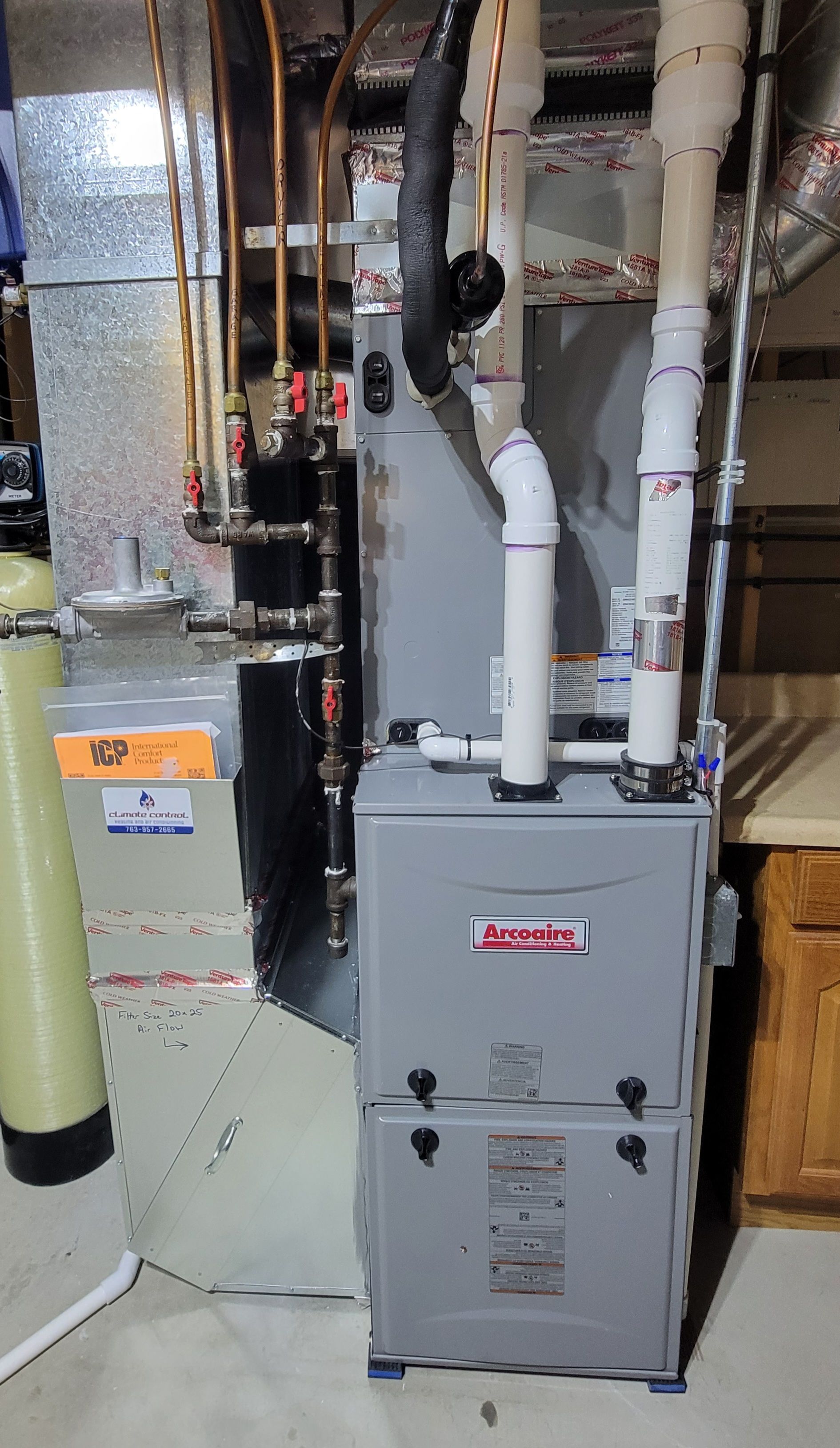 Furnace and water softener in a basement. Gray Lennox furnace with white pipes and a green water softener.