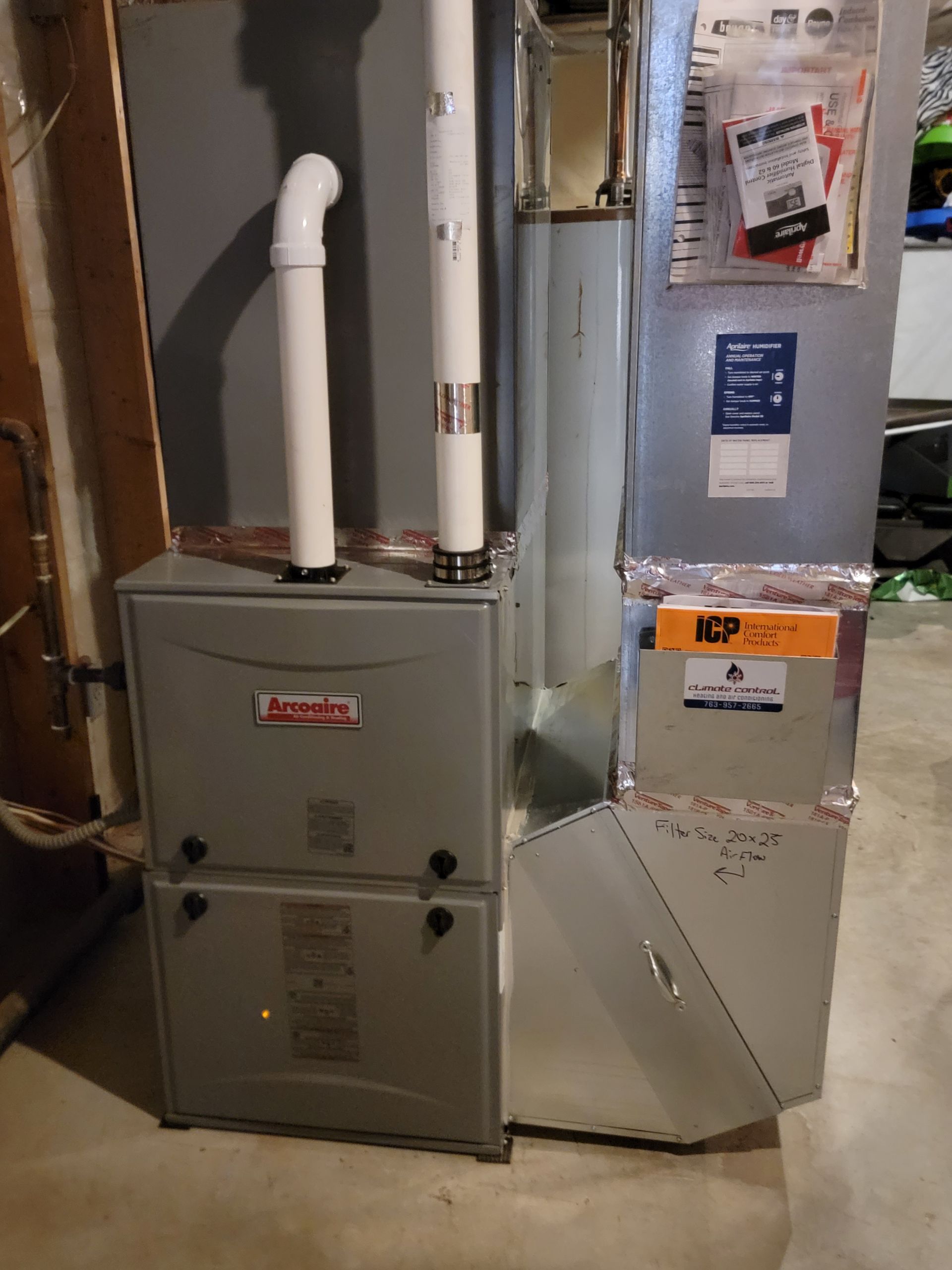 A gray Lennox furnace with white exhaust pipes in a basement setting.