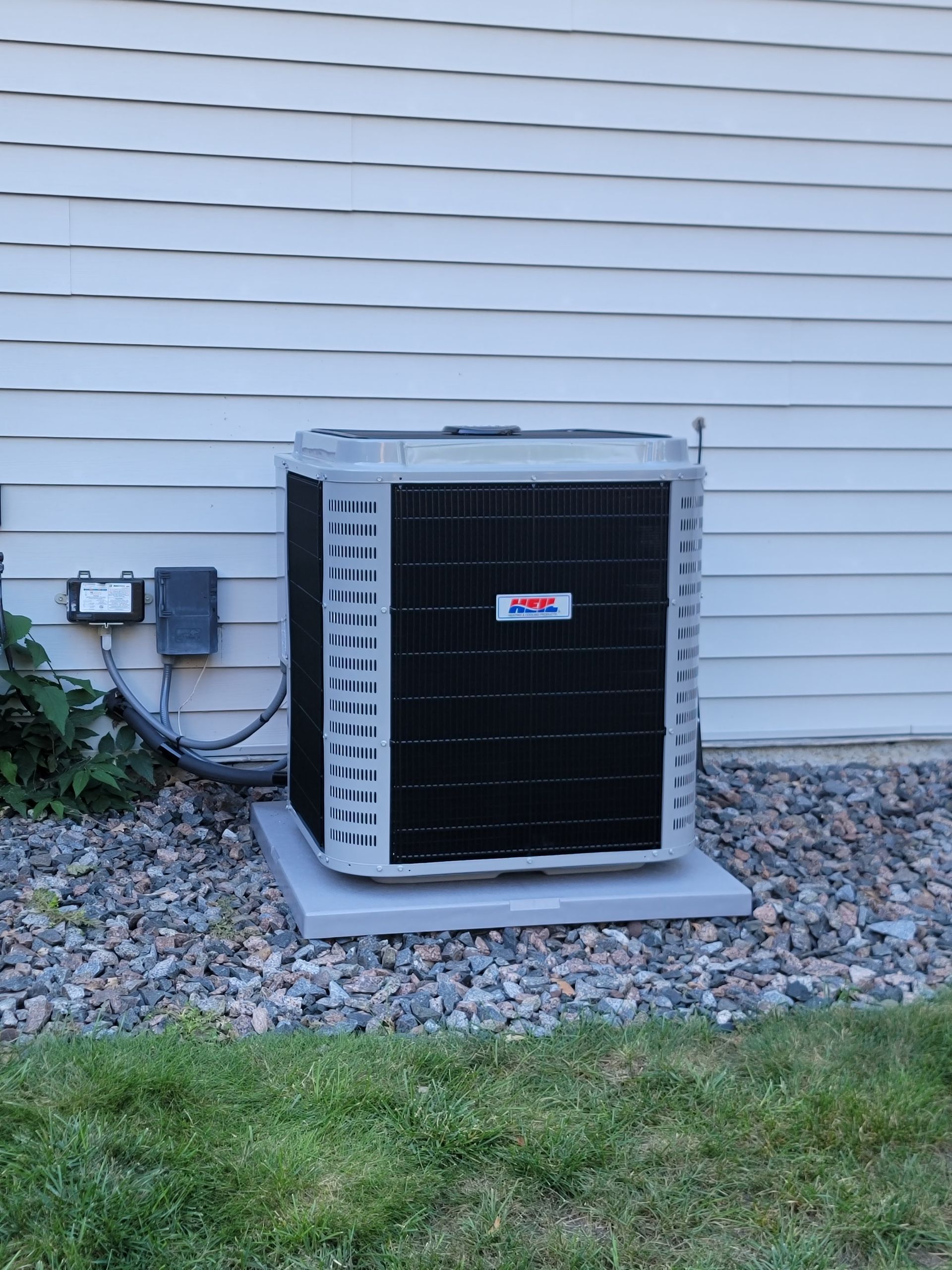 AC unit outside, gray and black, on a concrete pad, near a house with light gray siding.