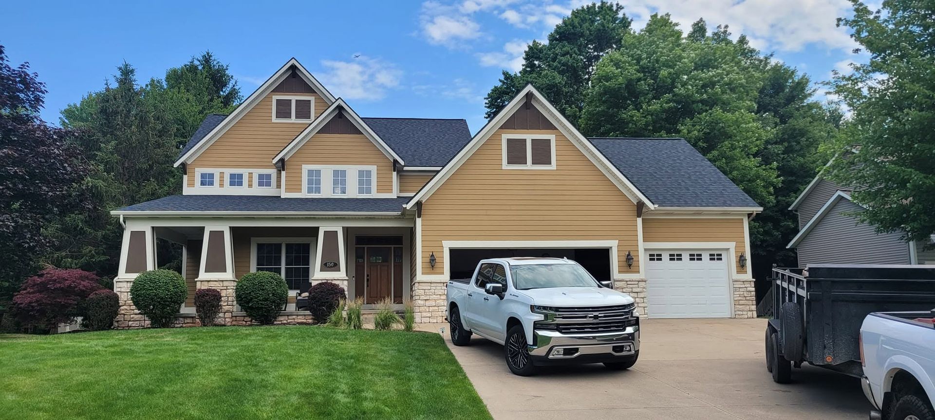 Suburban house with tan siding, white garage, black pickup truck, and green lawn under a blue sky