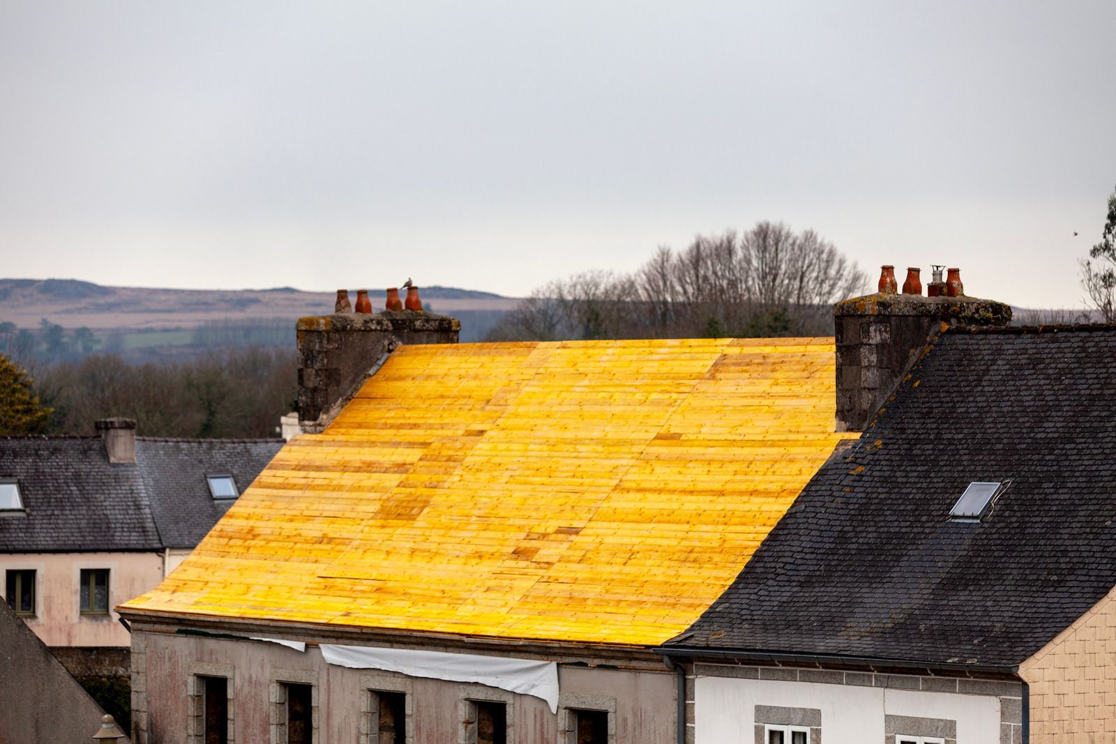Roof under repair with bright yellow tarp on a row of houses, under a cloudy sky
