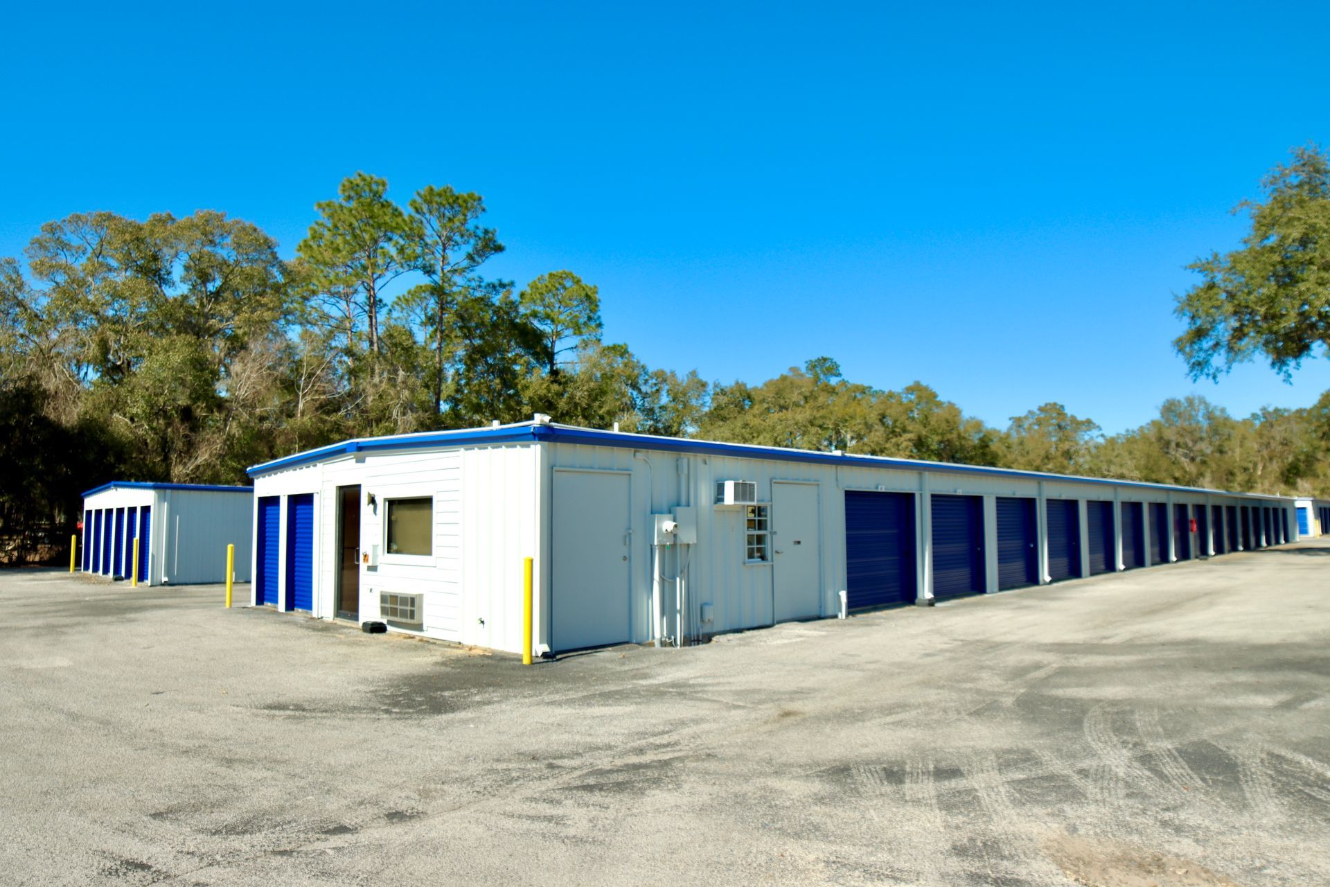 Storage units building with white walls, blue doors, and a clear sky.