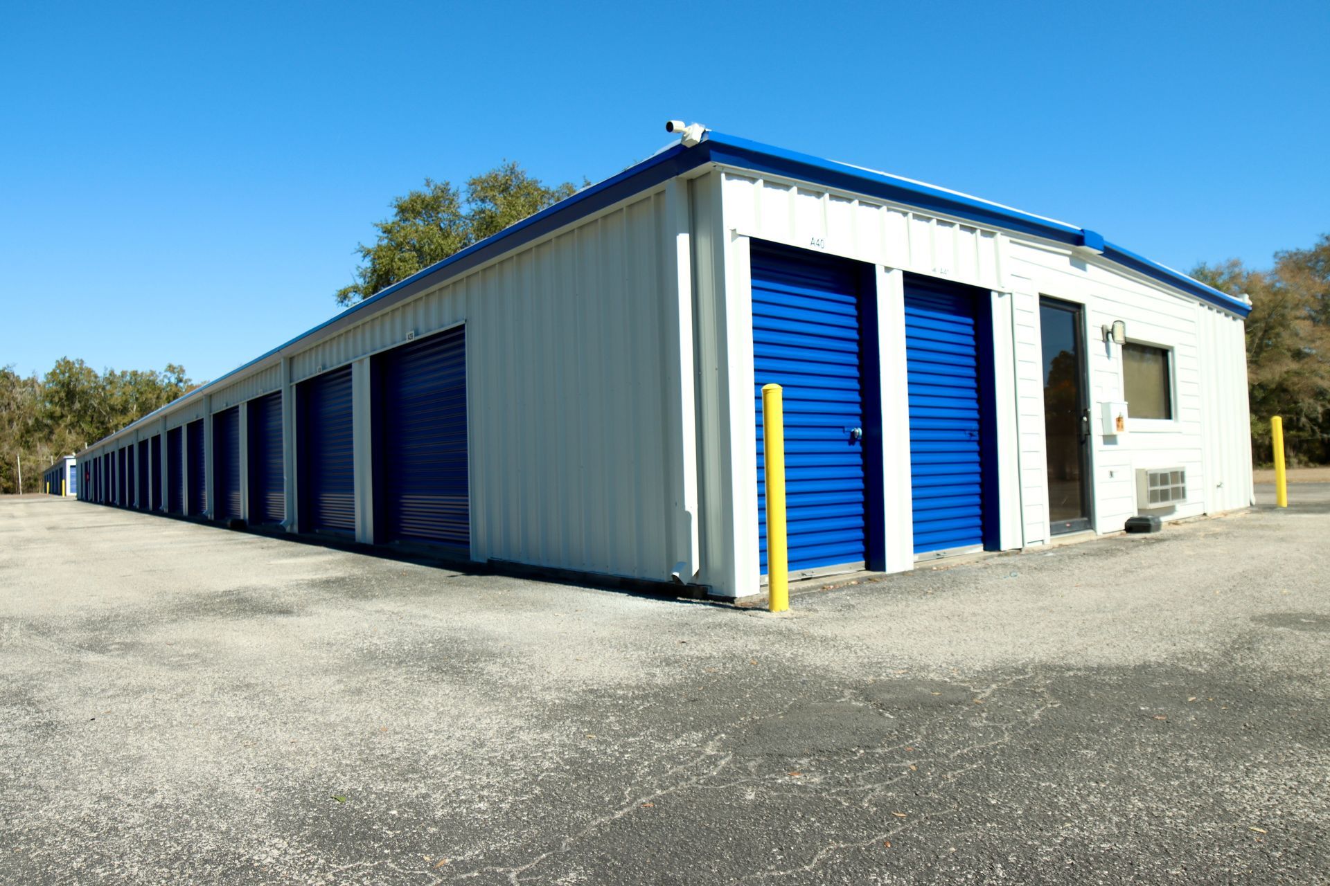 Storage units with blue doors, white metal siding, and a blue roof trim under a clear blue sky.