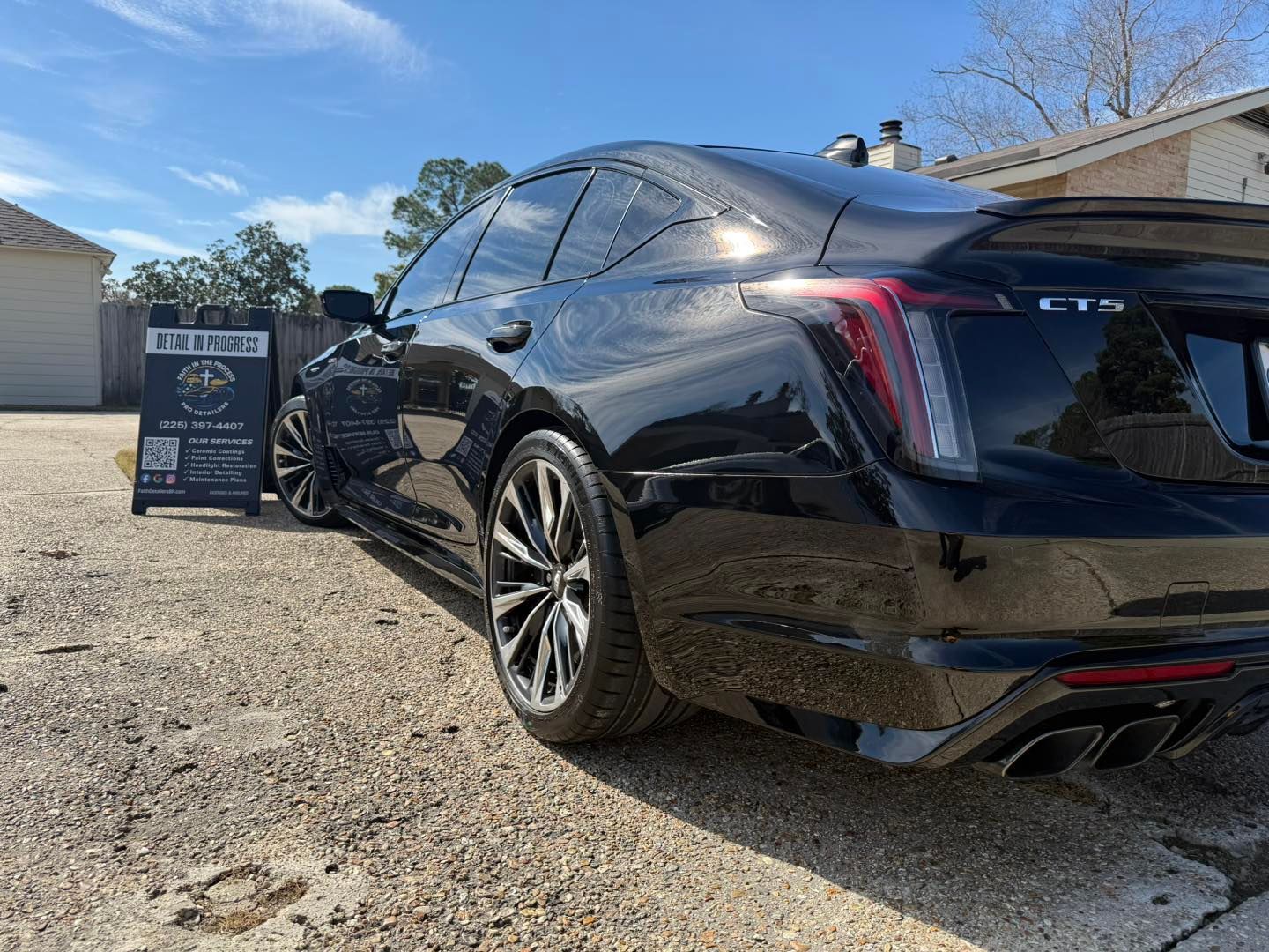 Black Cadillac sedan parked on gravel beside a chalkboard sign outside a building.