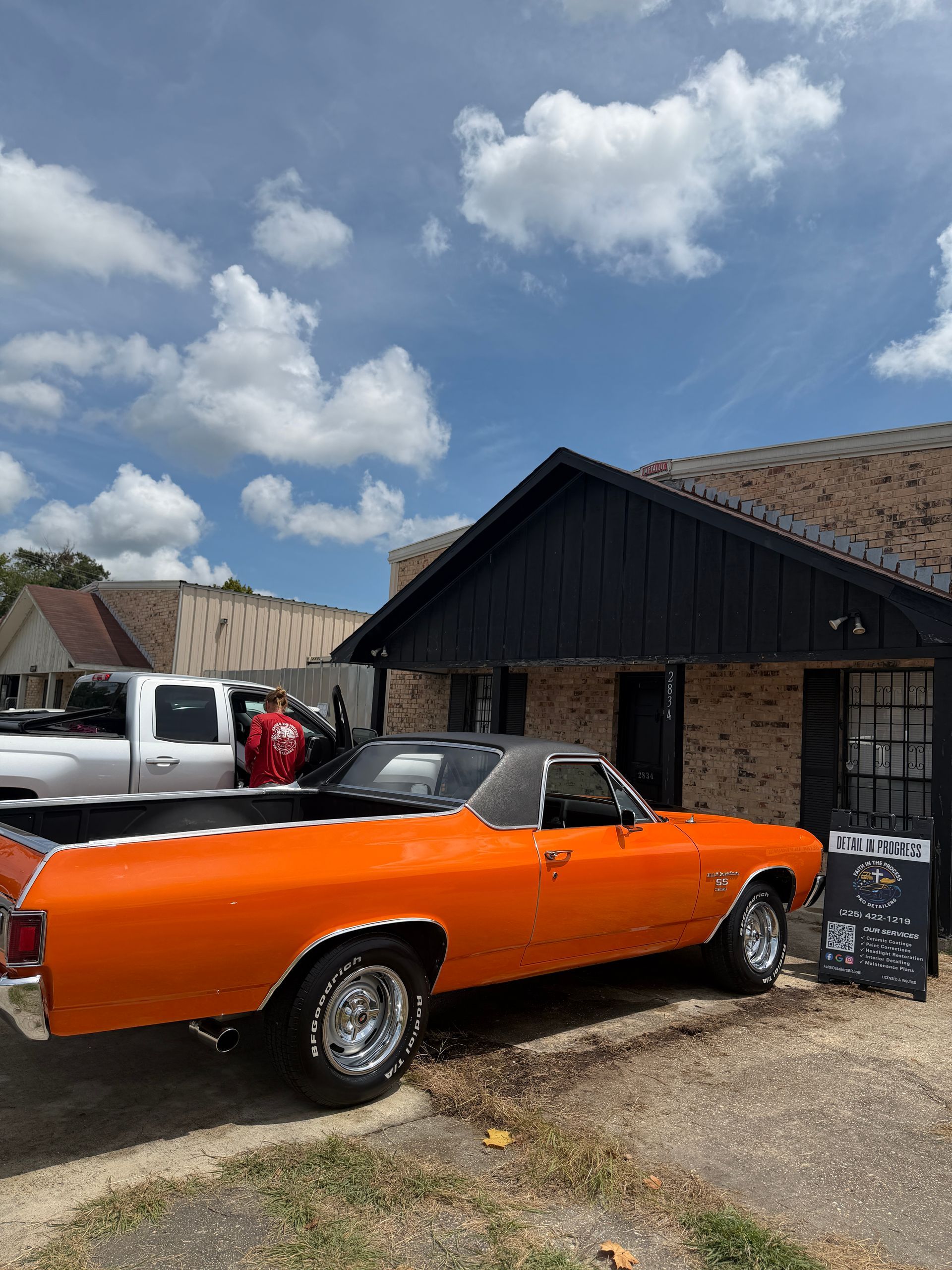 Orange vintage convertible parked outside a building under a partly cloudy sky
