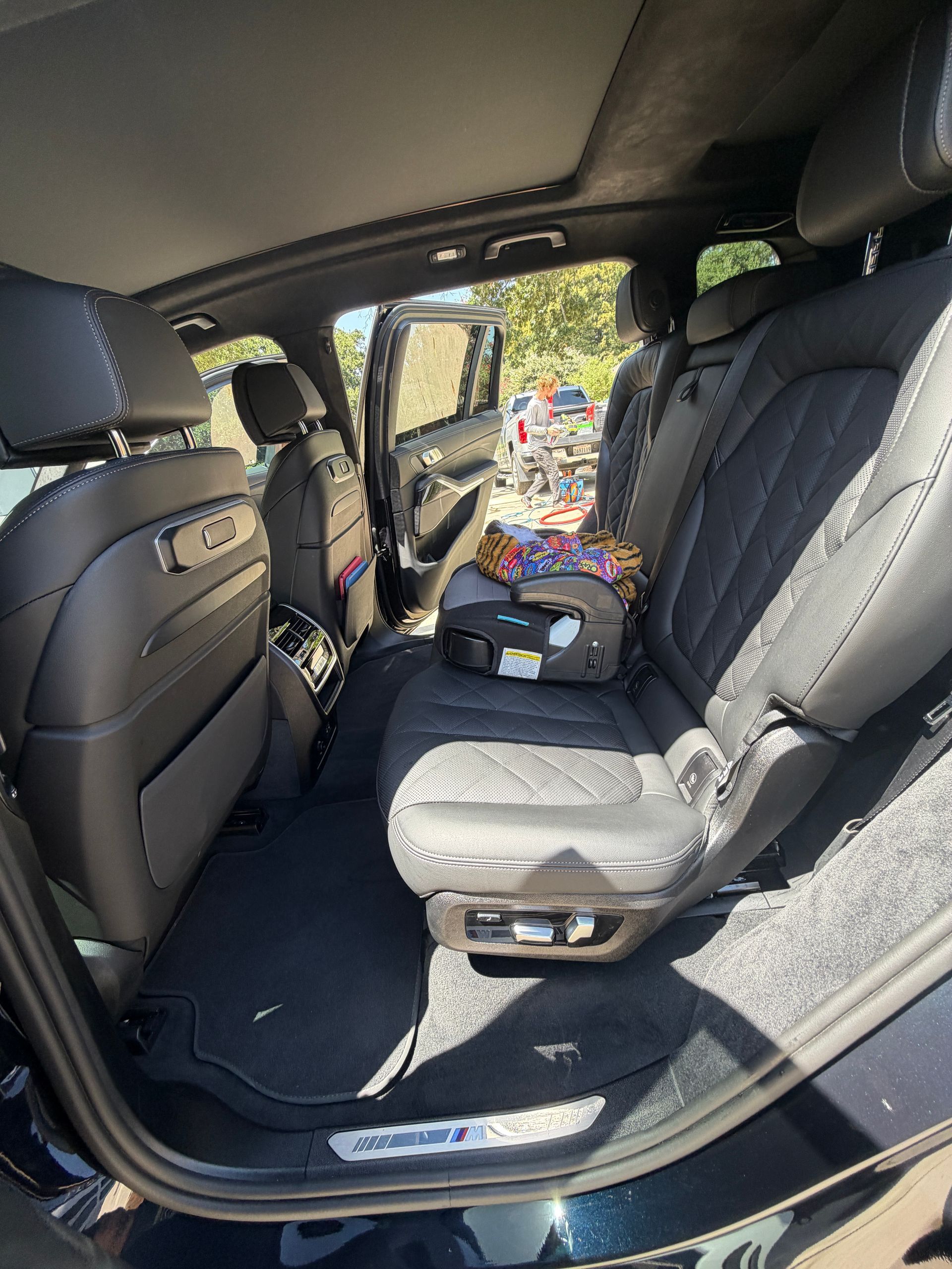 Empty SUV back seat with black leather seats and open door, showing the outdoors beyond.