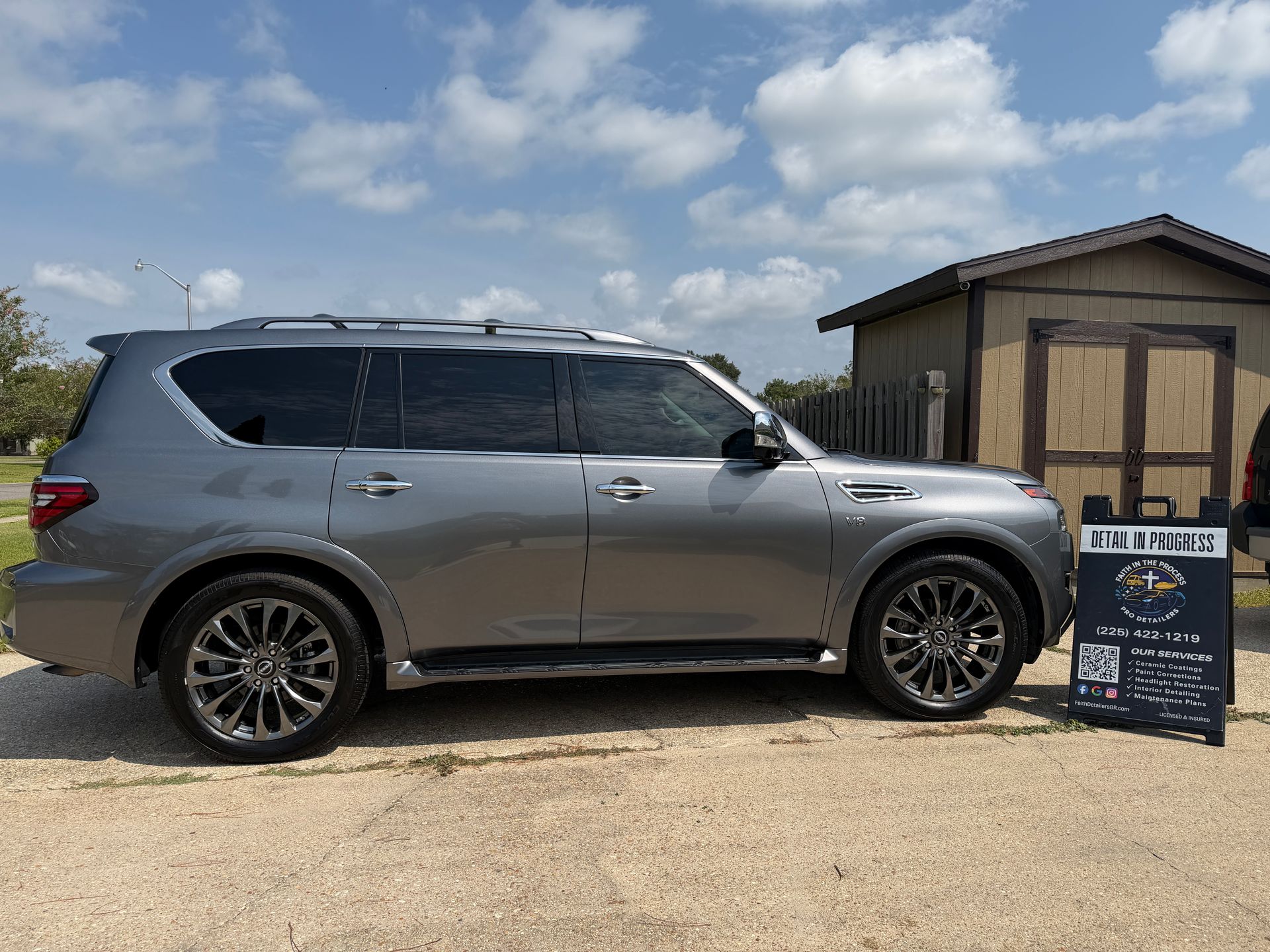 Gray SUV parked beside a small building with a sign in front, under a partly cloudy sky