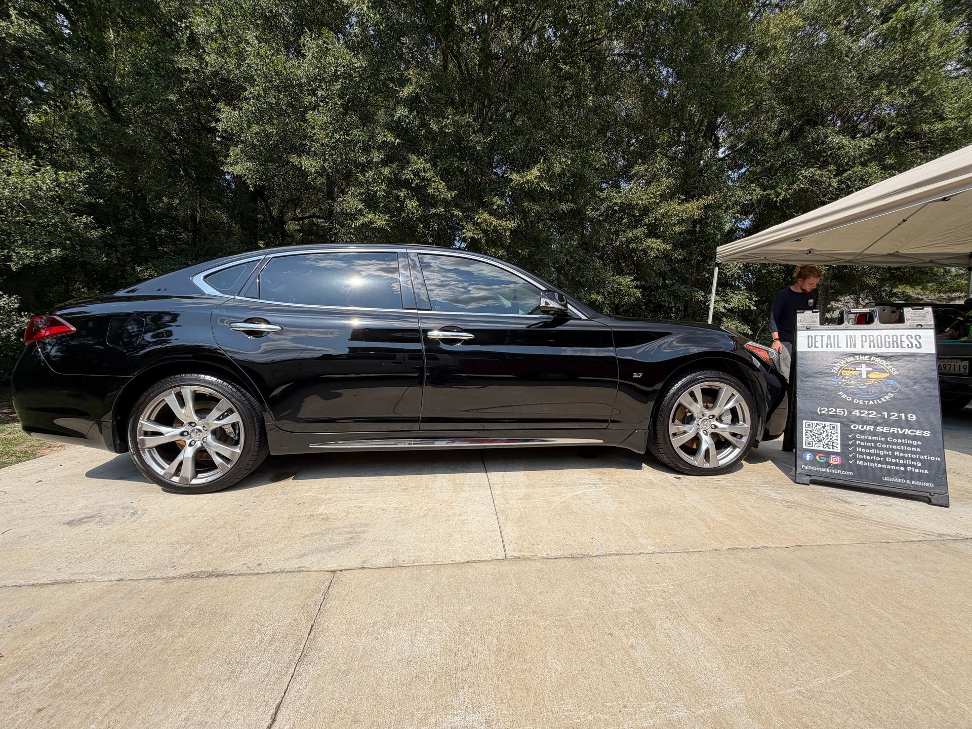 Black sedan parked beside a sidewalk sign outside a building with trees in the background