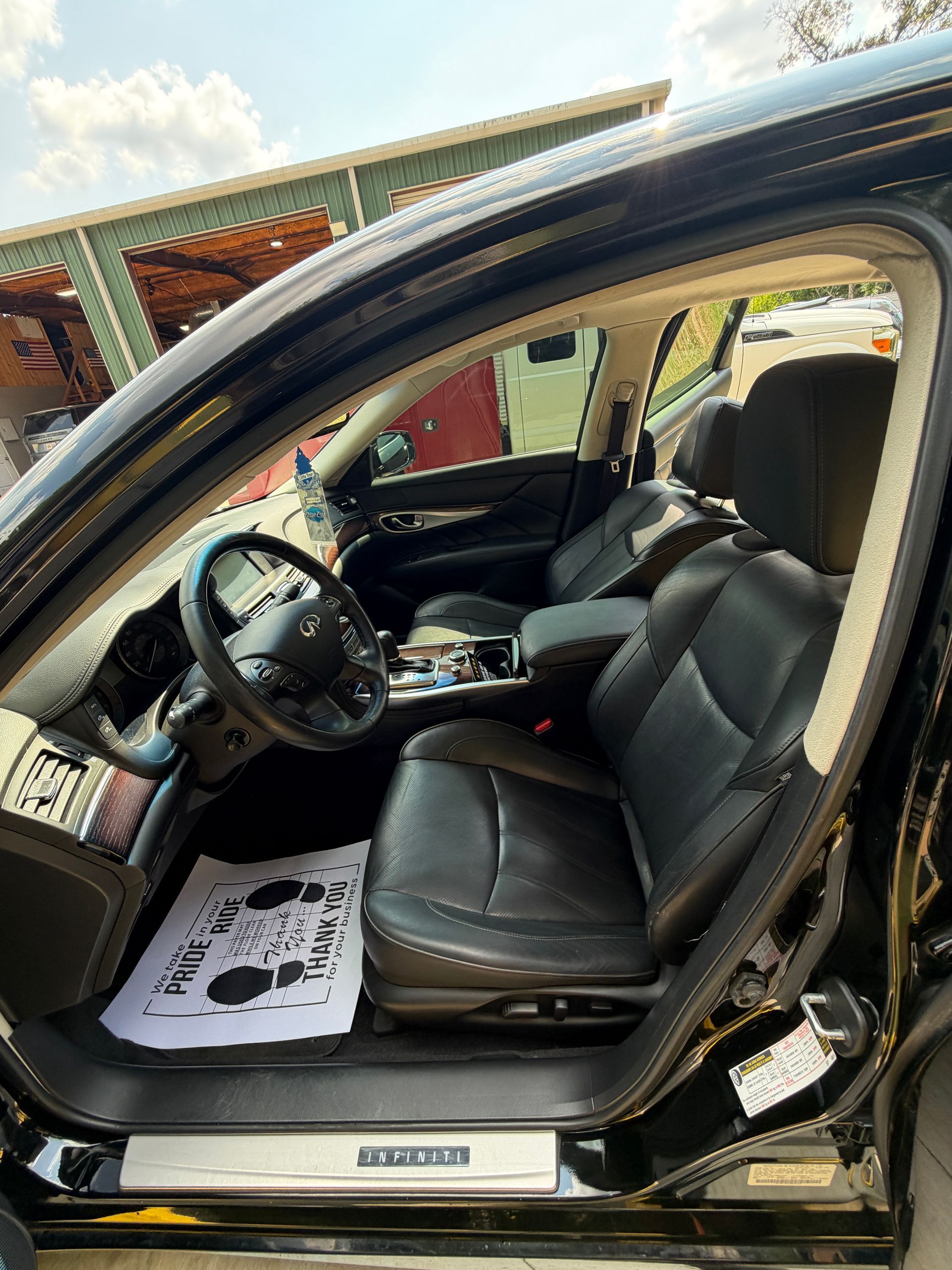 Open car door showing black leather interior and steering wheel, with a white floor mat on the driver’s side.