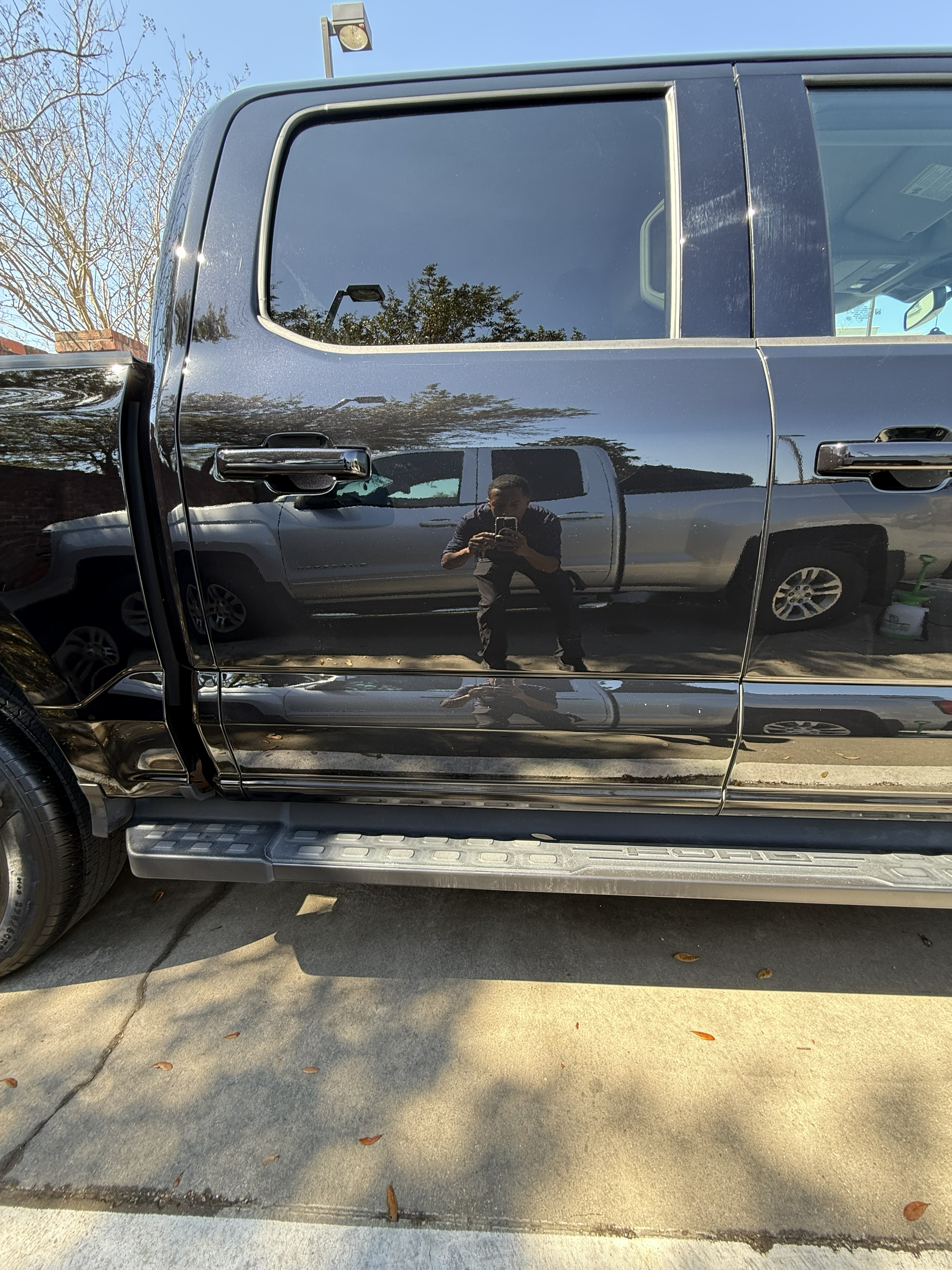 Black pickup truck side door with reflective paint parked outdoors on a sunny day