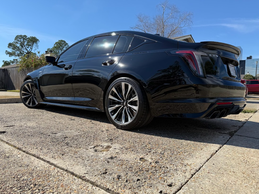 Black sedan parked on a concrete driveway under a clear blue sky