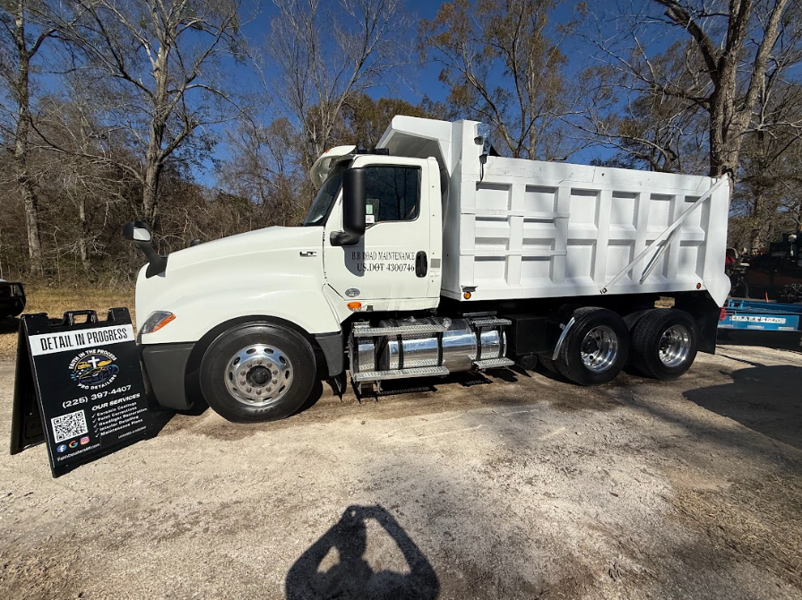 White dump truck parked outdoors beside a sales sign on a sunny day