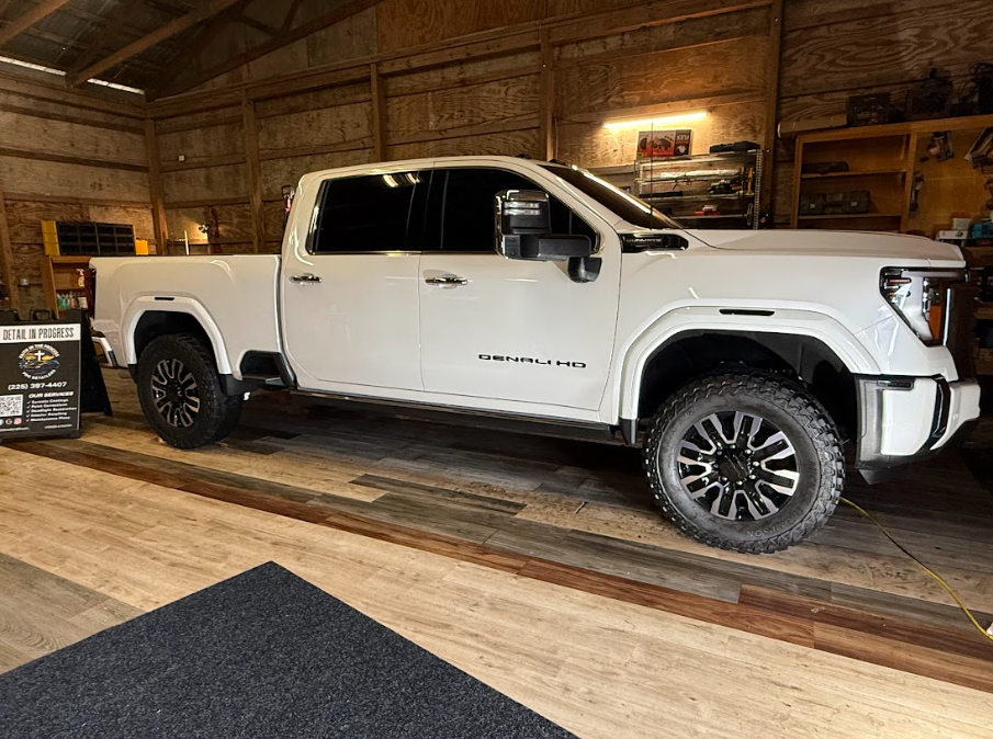 White pickup truck displayed indoors in a rustic showroom with wood walls and floor.