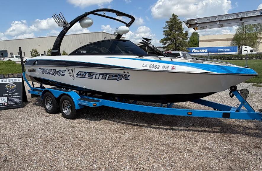 Blue and white wakeboard boat on a trailer at an outdoor marina lot