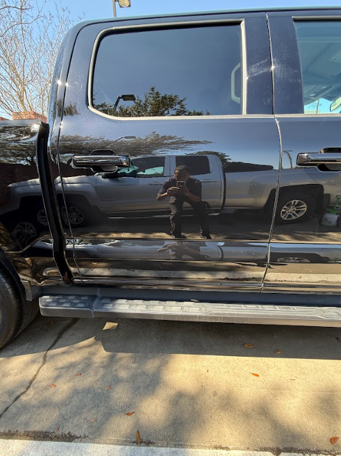 Black pickup truck with a dented rear door, parked in a driveway, reflecting a person taking the photo
