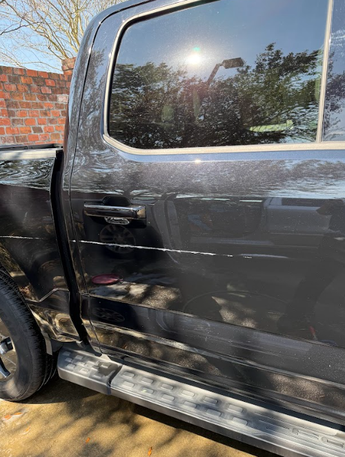 Black pickup truck side door with visible dents and scratches in daylight