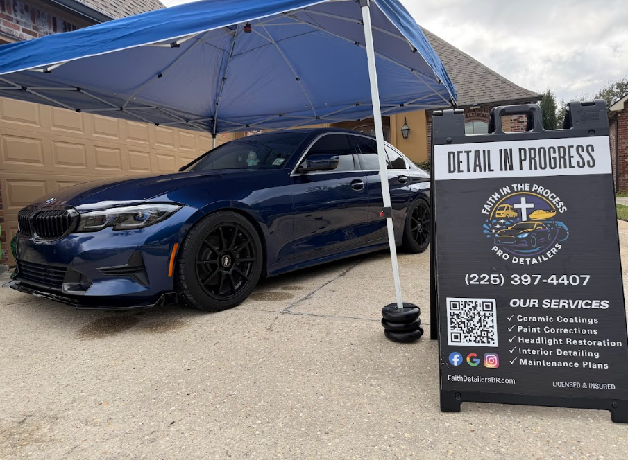 Blue sports car under canopy beside sign reading “Detail in Progress” at an auto detailing shop