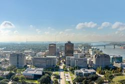 City skyline with mid-rise buildings by a river under a bright blue sky with clouds