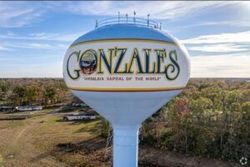 Gonzales city water tower with logo against a cloudy sky and trees below