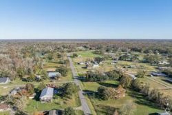 Aerial view of a suburban neighborhood with roads, houses, trees, and open green spaces under a blue sky