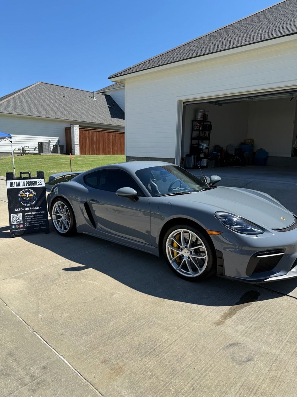 Silver sports car parked in a driveway outside an open garage on a sunny day