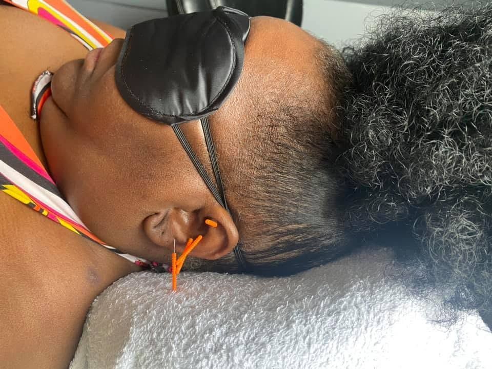 Close-up of a person reclining with a black sleep mask and orange earrings, head resting on a pillow.