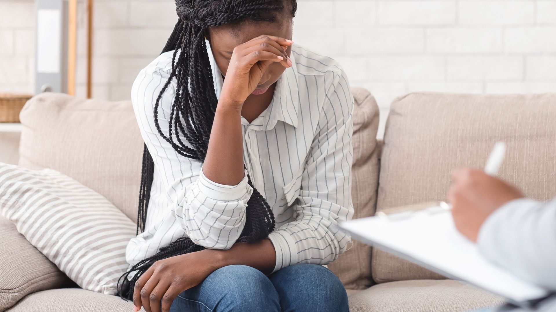 Woman on couch during therapy session, speaking with a counselor holding a notepad.