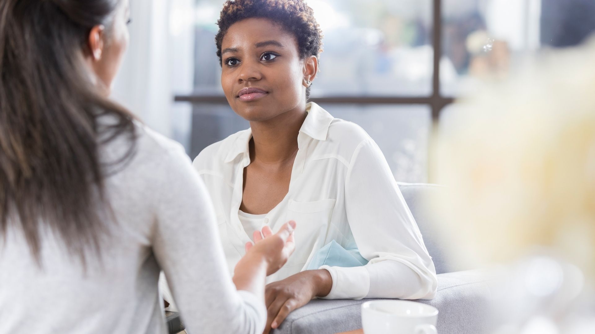 Two people talking in a bright office, one gesturing while seated across from the other.