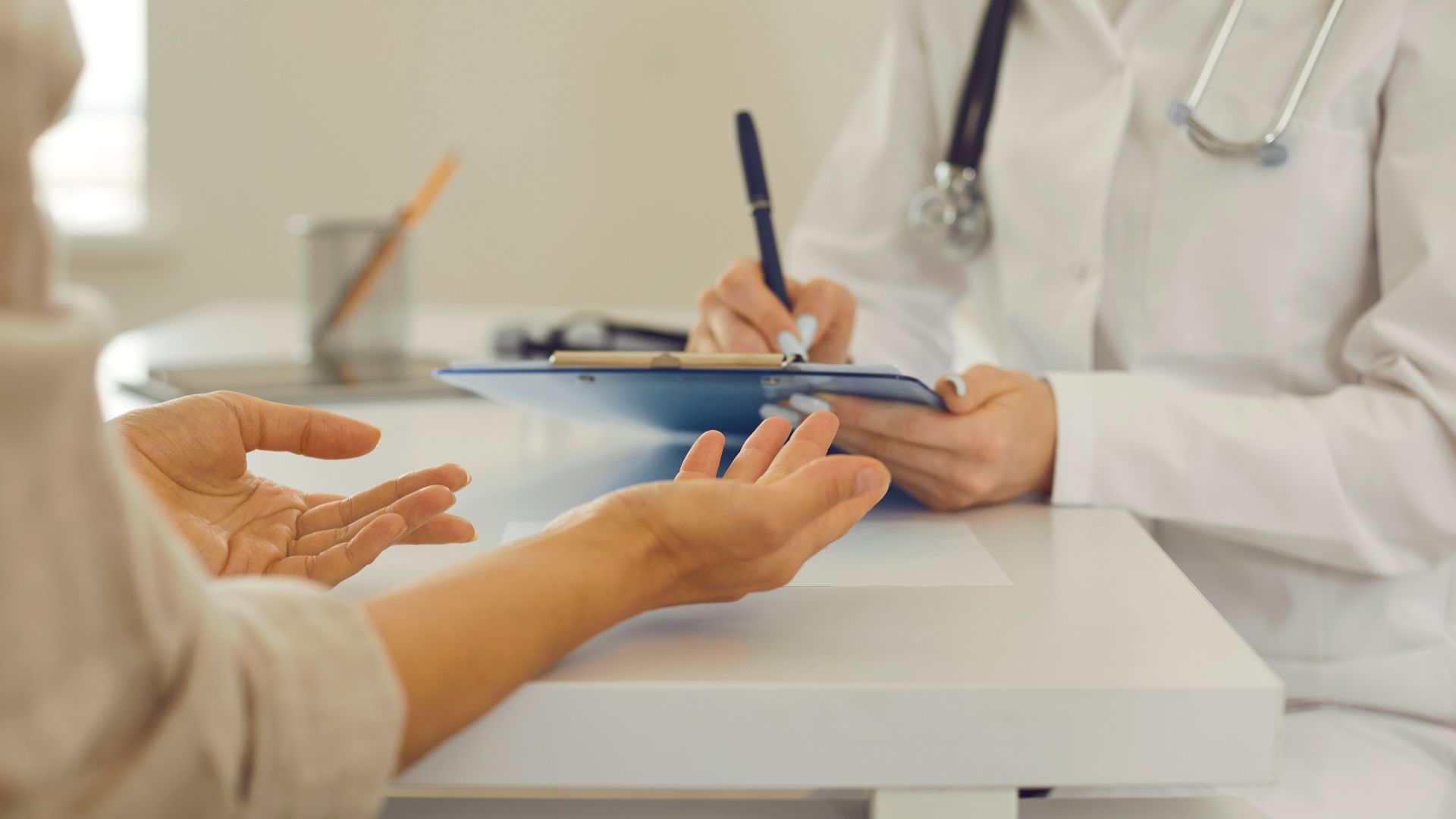 Doctor consulting with a patient, taking notes on a clipboard across a desk
