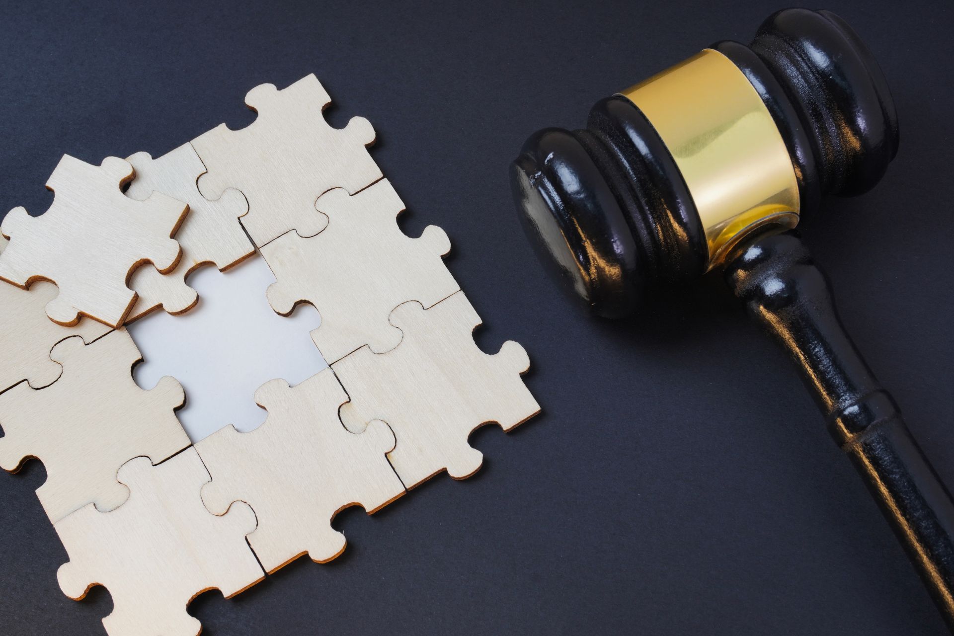 Jigsaw puzzle pieces next to a judge’s gavel on a dark background Jigsaw puzzle pieces next to a judge’s gavel on a dark background