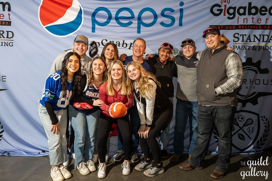 A group of people are posing for a picture in front of a pepsi sign.