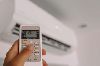 Hand holding an AC remote pointed at a wall-mounted air conditioner