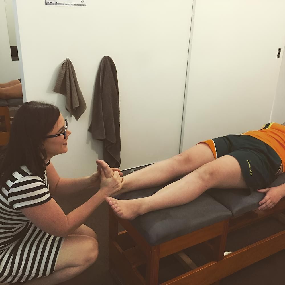 A Woman In A Striped Dress Is Touching A Woman 's Foot On A Table — Grays Chiropractic Centre In Rural View, QLD
