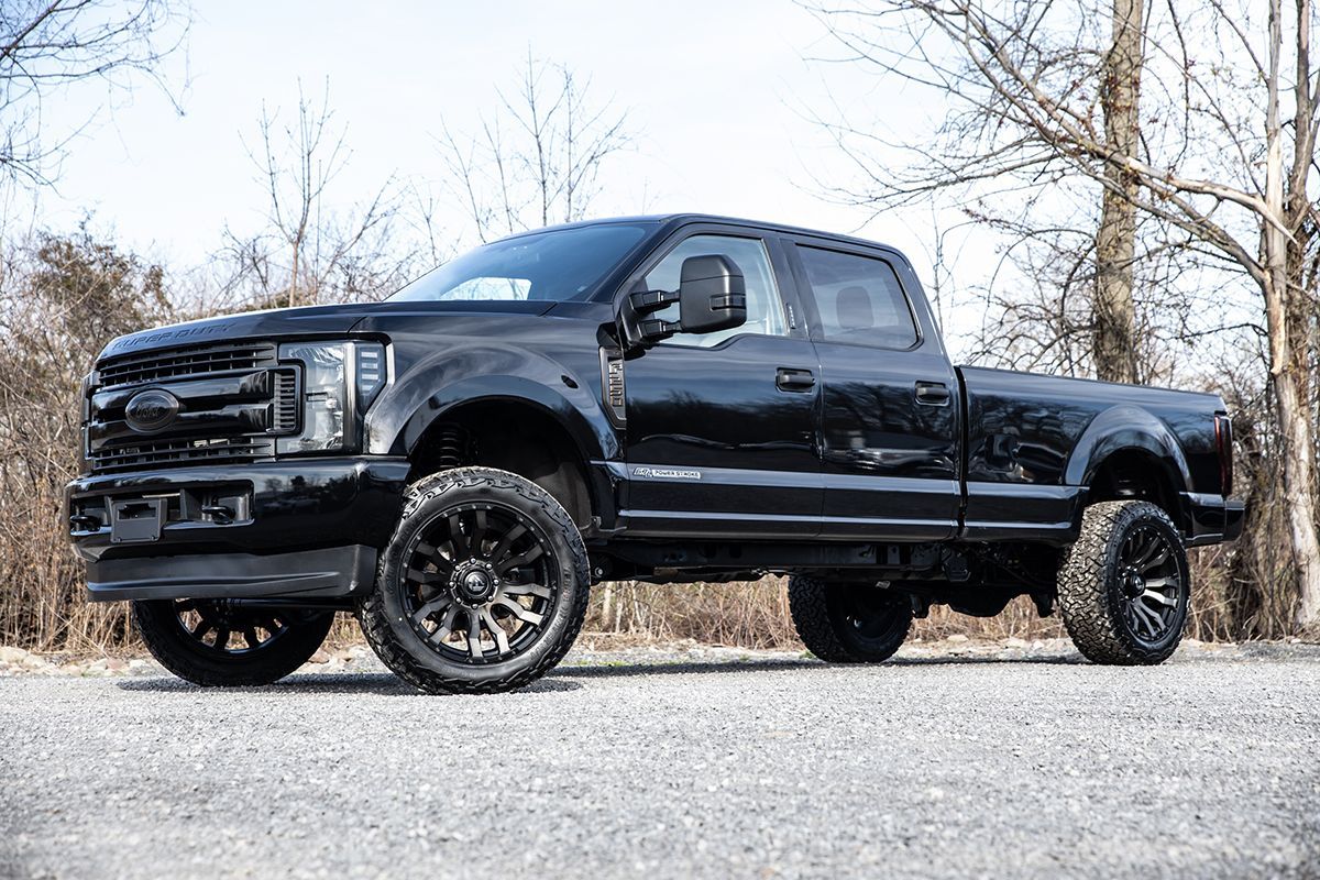 Black lifted pickup truck parked on gravel with trees in the background.