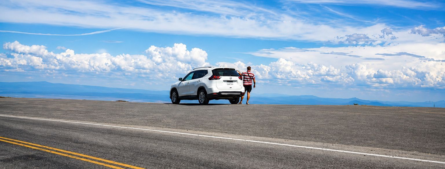 White SUV parked on a wide road with one person standing beside it under a blue sky
