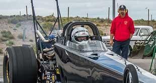 A man in a red hoodie is standing next to a race car.