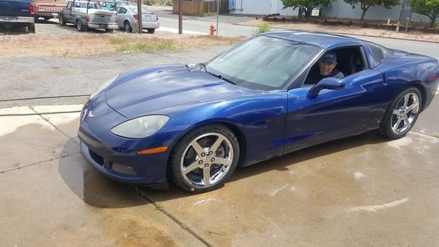A man is driving a blue sports car in a parking lot.
