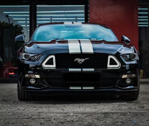 A black Ford Mustang with silver racing stripes parked in front of a building.