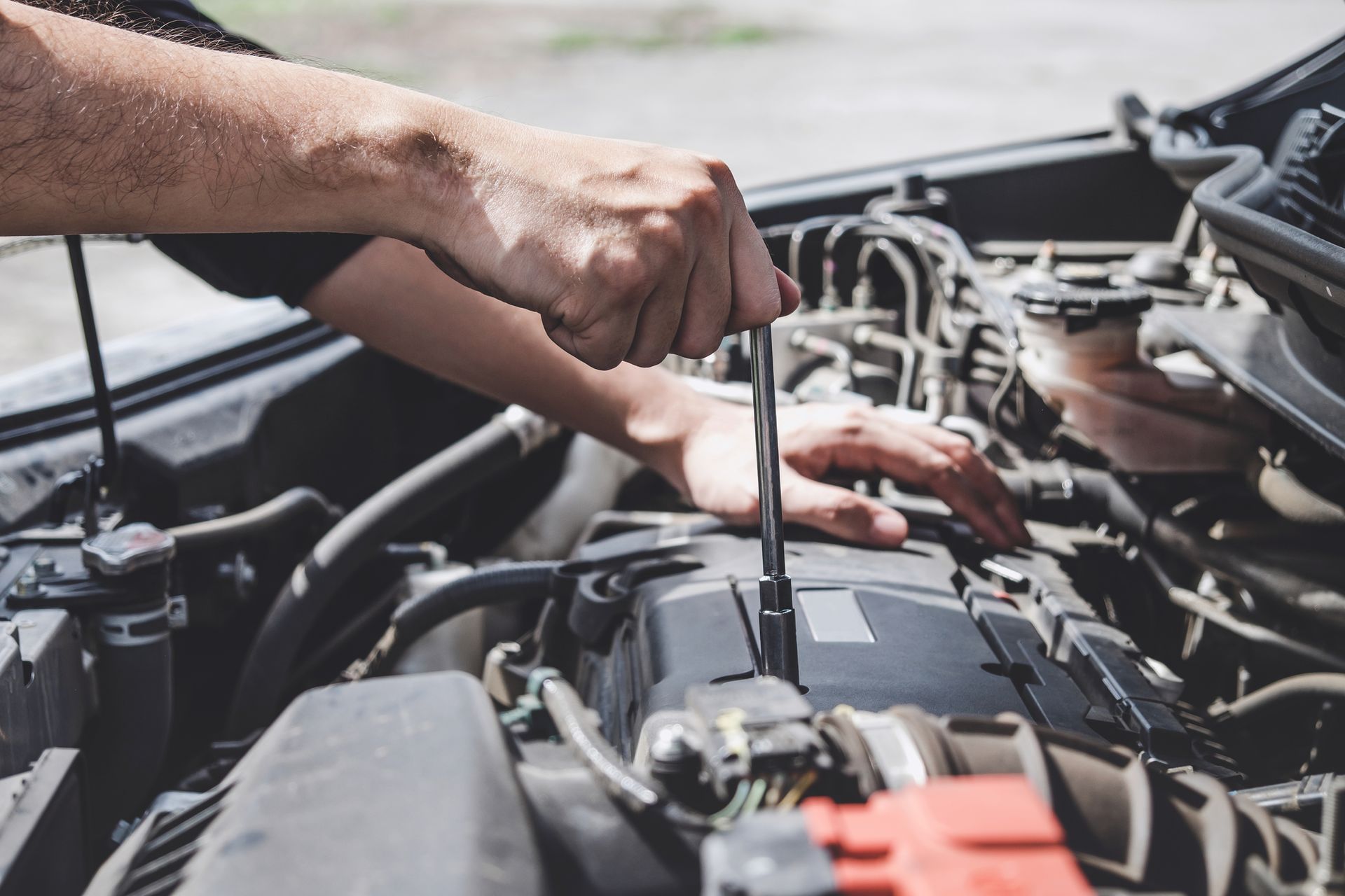 A man is working on the engine of a car with a screwdriver.