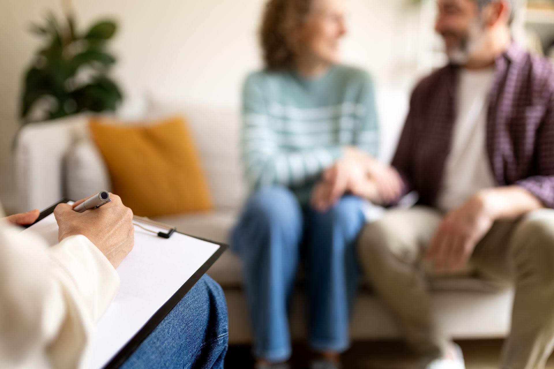 Therapist taking notes on a clipboard with a smiling couple blurred in the background. Therapist taking notes on a clipboard with a smiling couple blurred in the background.